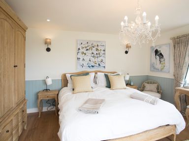 A bedroom with a wooden bed and white bedding two nightstands a chandelier and paintings on the walls at Penrhyn Barn in Dulas