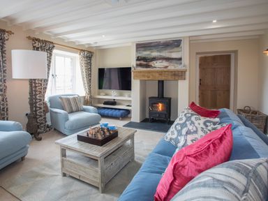 A living room with blue chairs a wooden coffee table a chess set a fireplace and a television at Penrhyn Barn in Dulas