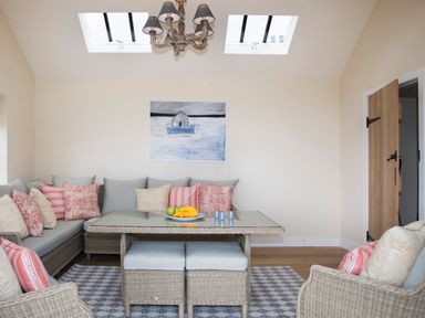 A seating area with wicker furniture and cushions with a table and chandelier at Penrhyn Barn in Dulas