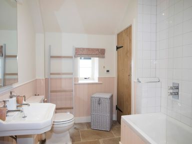 A bathroom with a sink toilet laundry basket bathtub and wooden door at Penrhyn Barn in Dulas