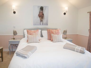 A bedroom with a double bed white bedding and pink patterned pillows two bedside tables with lamps and a painting above the bed at Penrhyn Barn in Dulas