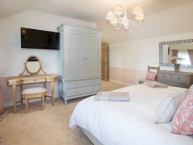 A bedroom with a bed a wardrobe a dressing table a chest of drawers and a wall mounted tv at Penrhyn Barn in Dulas