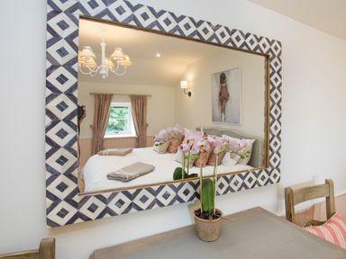 A mirror reflecting a bedroom with a bed pillows and window with curtains at Penrhyn Barn in Dulas