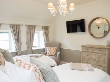 A bedroom with two beds an armchair a wooden dresser a wall-mounted TV and a round mirror at Penrhyn Barn in Dulas