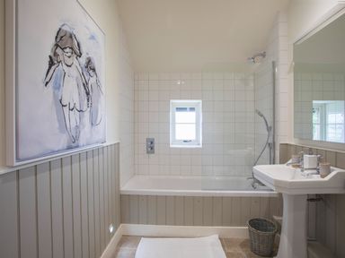 A bathroom with a bathtub shower sink mirror painting and a small window at Penrhyn Barn in Dulas