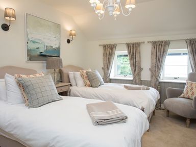 A bedroom with two single beds with pillows and folded blankets and an armchair near windows with curtains at Penrhyn Barn in Dulas