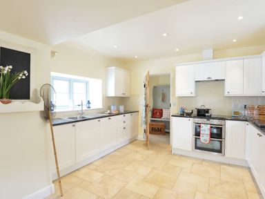 A kitchen with white cabinets, black countertops, a double oven, a window above the sink, and a doorway leading to another room at Penrhyn Farm in Moelfre