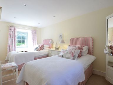 A bedroom with two single beds with striped headboards and floral cushions at Penrhyn Farm in Moelfre