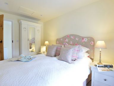 A bedroom with a bed with floral and striped pillows two bedside tables with lamps an open door and a white wardrobe with a mirror at Penrhyn Farm in Moelfre