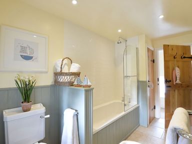 A bathroom with a bathtub shower combination a toilet with a potted plant on top and a wooden door with hanging decorations at Penrhyn Farm in Moelfre