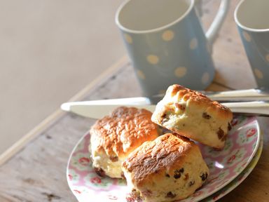 Three scones on a floral plate with two blue polka dot mugs and knives on a wooden table at Penrhyn Farm in Moelfre