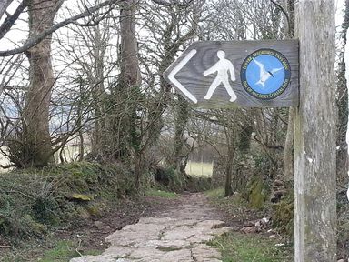 A footpath with a wooden signpost showing a walking route for the Isle of Anglesey Coastal Path at Penrhyn Farm in Moelfre