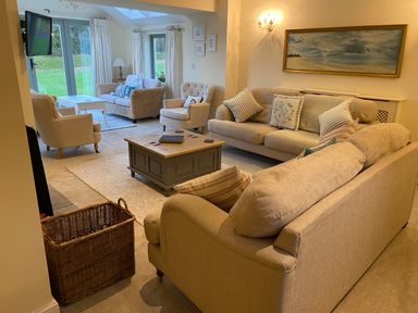 A living room with beige sofas a wooden coffee table and large windows at Penrhyn Farm in Moelfre