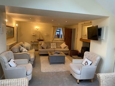 A living room with sofas armchairs a coffee table a wall-mounted TV and a fireplace at Penrhyn Farm Moelfre