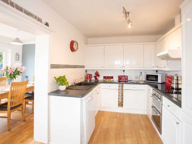 A kitchen with white cabinets black countertops and red appliances next to a dining area with a wooden table and chairs at Pen Y Daith in Aberffraw