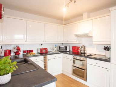 A kitchen with white cabinets black countertops red appliances and kitchenware at Pen Y Daith in Aberffraw