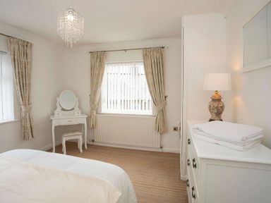 A bedroom with a bed a white dressing table with stool and a white chest of drawers with a lamp and folded towels at Pen Y Daith in Aberffraw