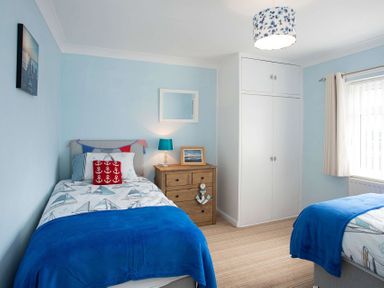 A bedroom with two single beds a wooden chest of drawers and a built in wardrobe at Pen Y Daith in Aberffraw