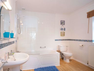 A bathroom with a bathtub shower combination a sink toilet and a blue bath mat at Pen Y Daith in Aberffraw