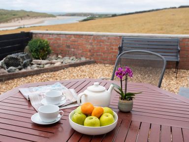 An outdoor wooden table with a bowl of fruit teapot two teacups and a small purple flower plant at Pen Y Daith in Aberffraw