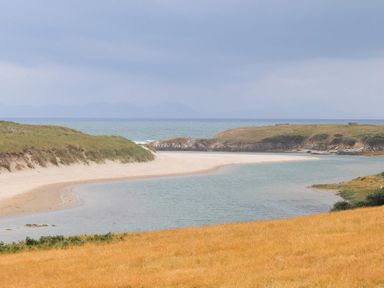 A sandy beach with a narrow water channel and grassy hills near the sea at Pen Y Daith in Aberffraw