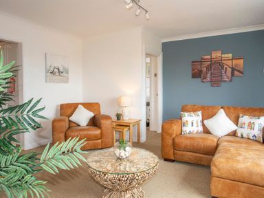 A living room with brown leather sofas a round wooden coffee table lamp and wall art at Pen Y Daith in Aberffraw