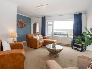 A living room with brown armchairs and a glass coffee table near a large window at Pen Y Daith in Aberffraw
