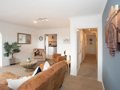 A living room with brown sofas a round coffee table a plant and a hallway at Pen Y Daith in Aberffraw