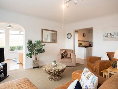 A living room with brown sofas a glass coffee table and a plant near an archway at Pen Y Daith in Aberffraw