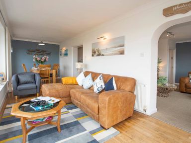 A living room with a brown sofa blue armchair wooden dining table and chairs at Pen Y Daith in Aberffraw