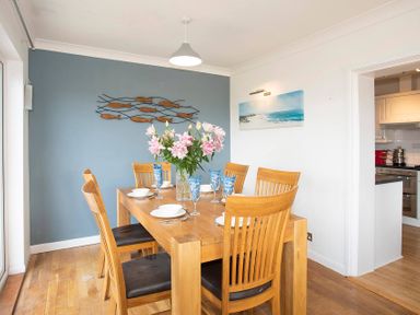 A dining room with a wooden table and six chairs with flowers on the table at Pen Y Daith in Aberffraw
