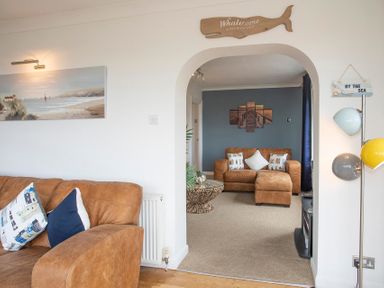 A living room with brown sofas and decorative pillows with a wooden whale sign above an archway at Pen Y Daith in Aberffraw