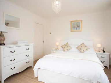 A bedroom with a bed two bedside tables a chest of drawers and a painting on the wall at Pen Y Daith in Aberffraw