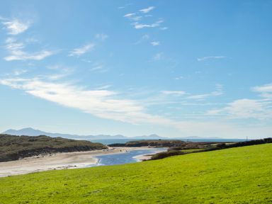 A coastal landscape with a sandy beach a water inlet green grassy field and distant mountains at Pen Y Daith in Aberffraw