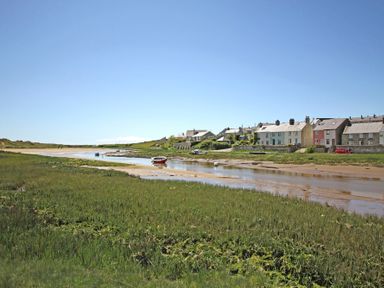 A river with boats and grassland beside houses under a clear sky at Pen Y Daith in Aberffraw