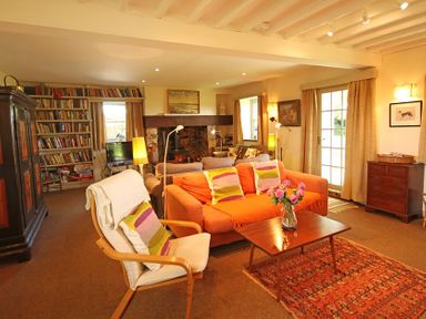 A living room with an orange sofa wooden chair coffee table with flowers fireplace bookshelf and carpet at Perth Hwfa in Malltraeth