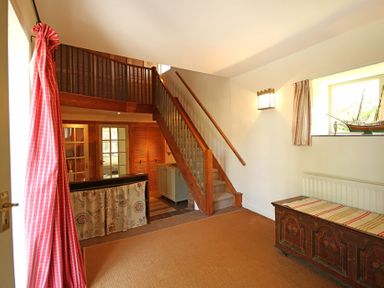 An interior space with carpeted floor wooden stairs wooden chest under a window and red curtains at Perth Hwfa in Malltraeth