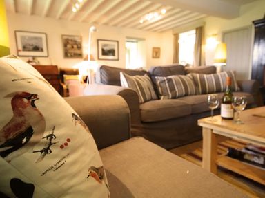 A living room with a beige sofa a cushion with bird prints a wooden coffee table with a wine bottle and glasses and framed pictures on the wall at Perth Hwfa in Malltraeth
