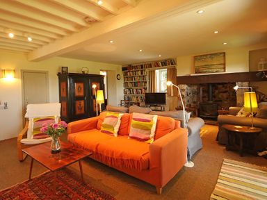 A living room with an orange sofa and a wooden table with flowers and bookshelves at Perth Hwfa in Malltraeth