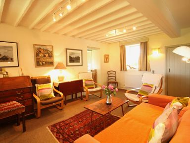 A living room with chairs a sofa a wooden coffee table with flowers a patterned rug and paintings on the wall at Perth Hwfa in Malltraeth