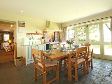 A kitchen dining area with wooden table and chairs set with dishes and a flower vase at Perth Hwfa in Malltraeth