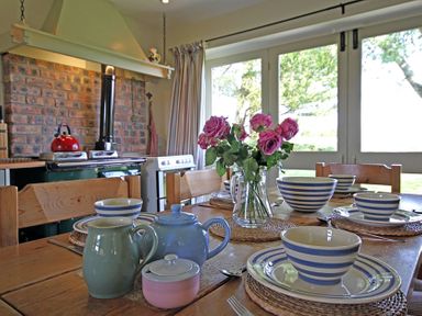 A dining table set with striped bowls plates and cups a teapot and pink flowers in a glass vase in a kitchen at Perth Hwfa in Malltraeth