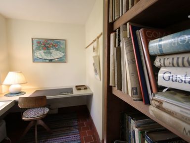 A study area with a wooden chair a desk lamp books on a shelf and a painting on the wall at Perth Hwfa in Malltraeth