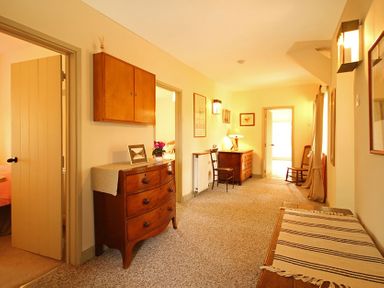 A hallway with wooden dressers chairs lamps and framed pictures at Perth Hwfa in Malltraeth