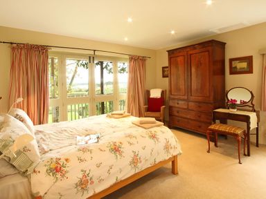 A bedroom with a floral bedspread a wooden wardrobe armchair and a dressing table at Perth Hwfa in Malltraeth