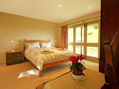 A bedroom with a wooden bed floral bedding bedside table and glass doors at Perth Hwfa in Malltraeth