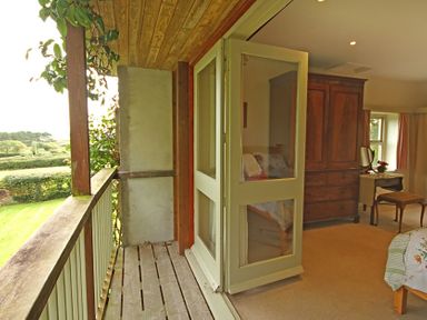 A bedroom with wooden wardrobe and vanity table opening onto a balcony with wooden railing at Perth Hwfa in Malltraeth