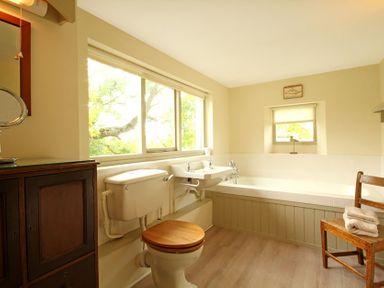 A bathroom with a toilet sink bathtub wooden chair cabinet and two windows at Perth Hwfa in Malltraeth