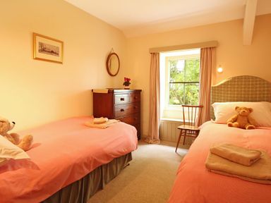 A bedroom with two single beds with orange bedding a wooden chair a chest of drawers and a window at Perth Hwfa in Malltraeth