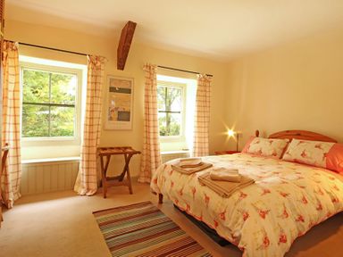 A bedroom with a double bed two windows with checked curtains and a wooden luggage rack at Perth Hwfa in Malltraeth